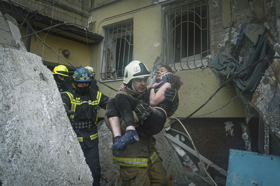A firefighter carries a wounded woman out of the rubble of a building.