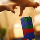 Two children's hands grab for a tower of LEGOs. 