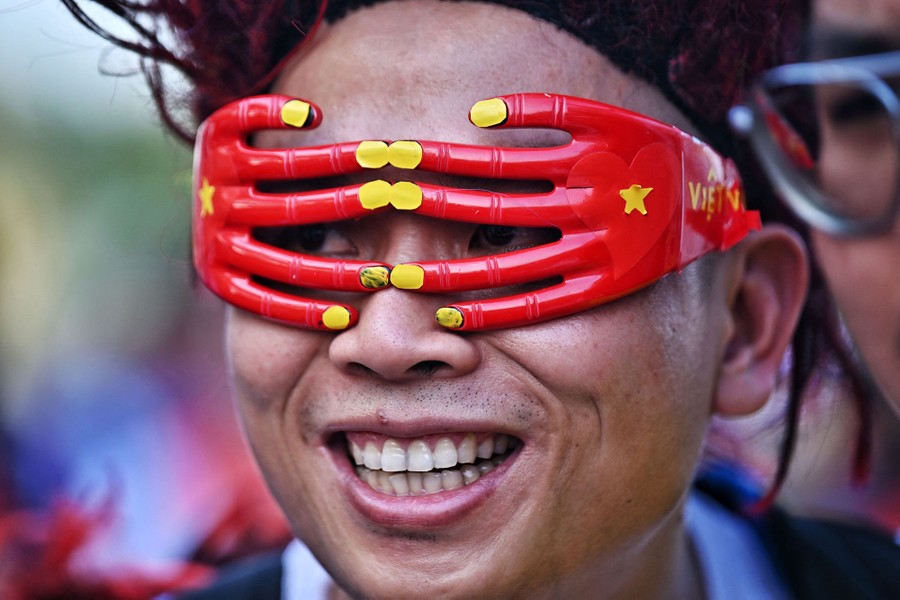 A Vietnamese soccer fan wears novelty glasses shaped like two hands painted in the colors of the Vietnamese flag.
