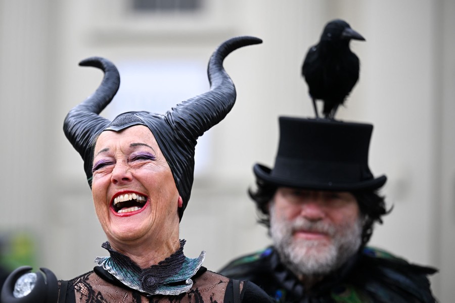 A person wearing a horned hat laughs as another person stands behind them wearing a flat-topped hat with a fake crow attached to it.