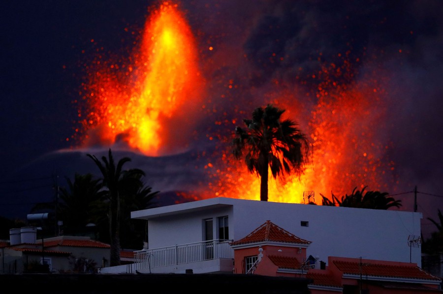 Lava jets erupt into the air behind several houses.
