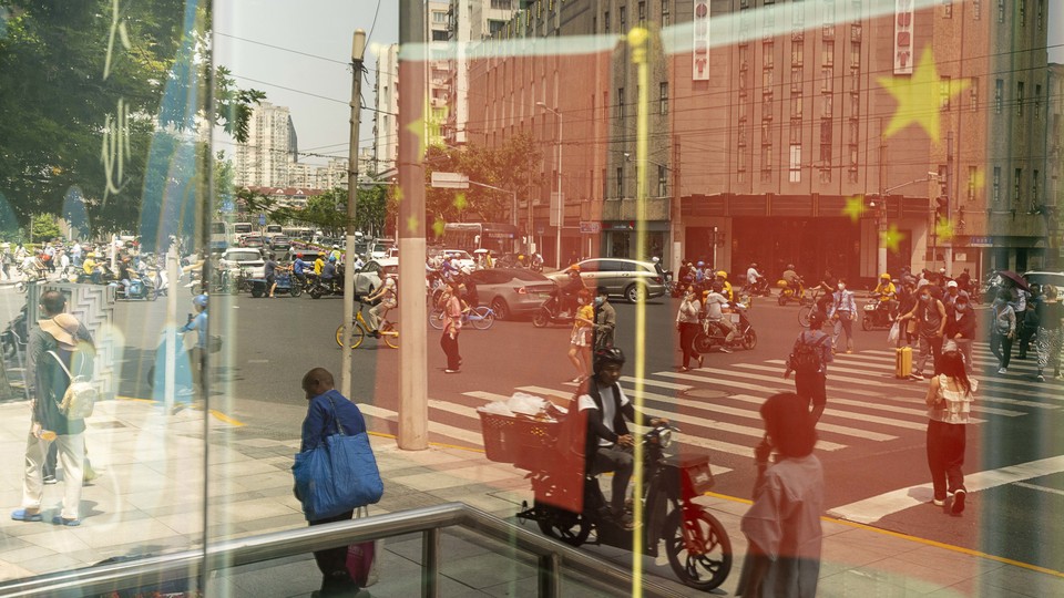 Chinese flags and pedestrians reflected in a window in Shanghai, China