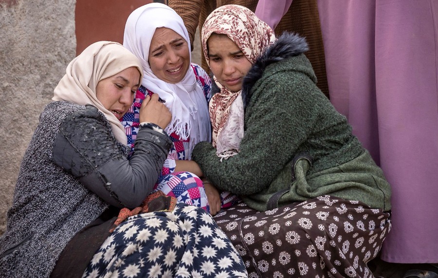 Three women cry while holding one another close.