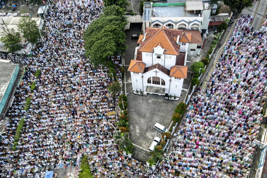 An aerial view of many people praying, kneeling in rows across roads at an intersection.