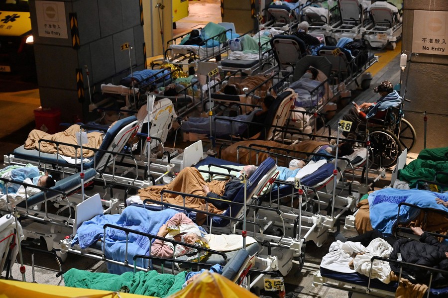 Dozens of people lie in hospital beds that are arranged just outside a hospital.