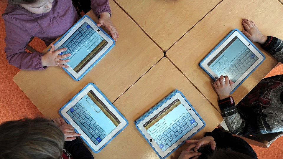 Children sit a table using tablet computers