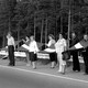 A group of people stand in a line holding hands with Latvian flags.