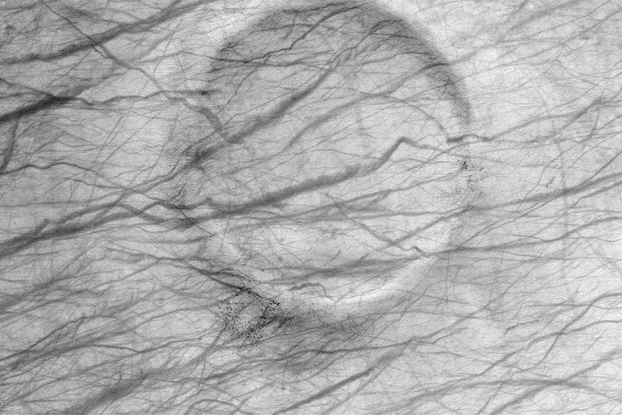An orbital view of horizontal dark streaks crossing an aging, eroded crater on Mars.