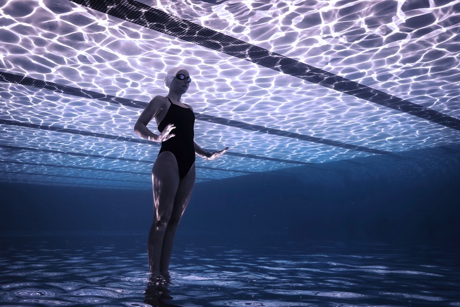 The photograph is upside-down. A person is seen underwater in a swimming pool, appearing to "stand" on the water's surface.
