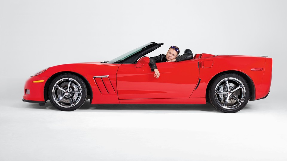 A man site in a red convertible with a sad expression on his face.