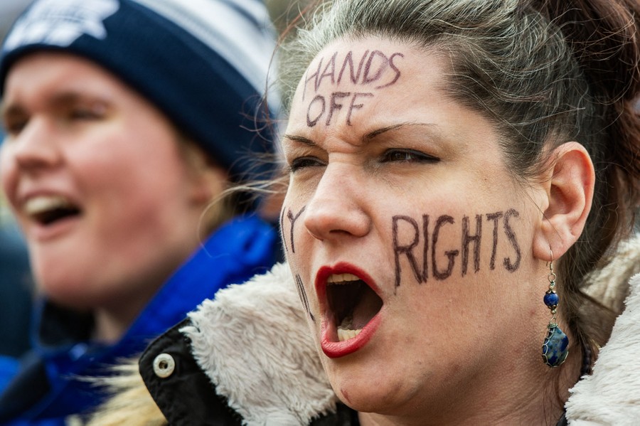 A protester shouts, a message written on her face reads 
