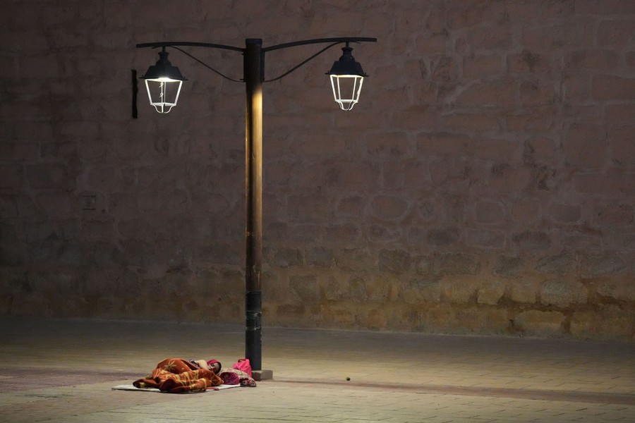 A person sleeps on a mat on the ground beneath a street light.