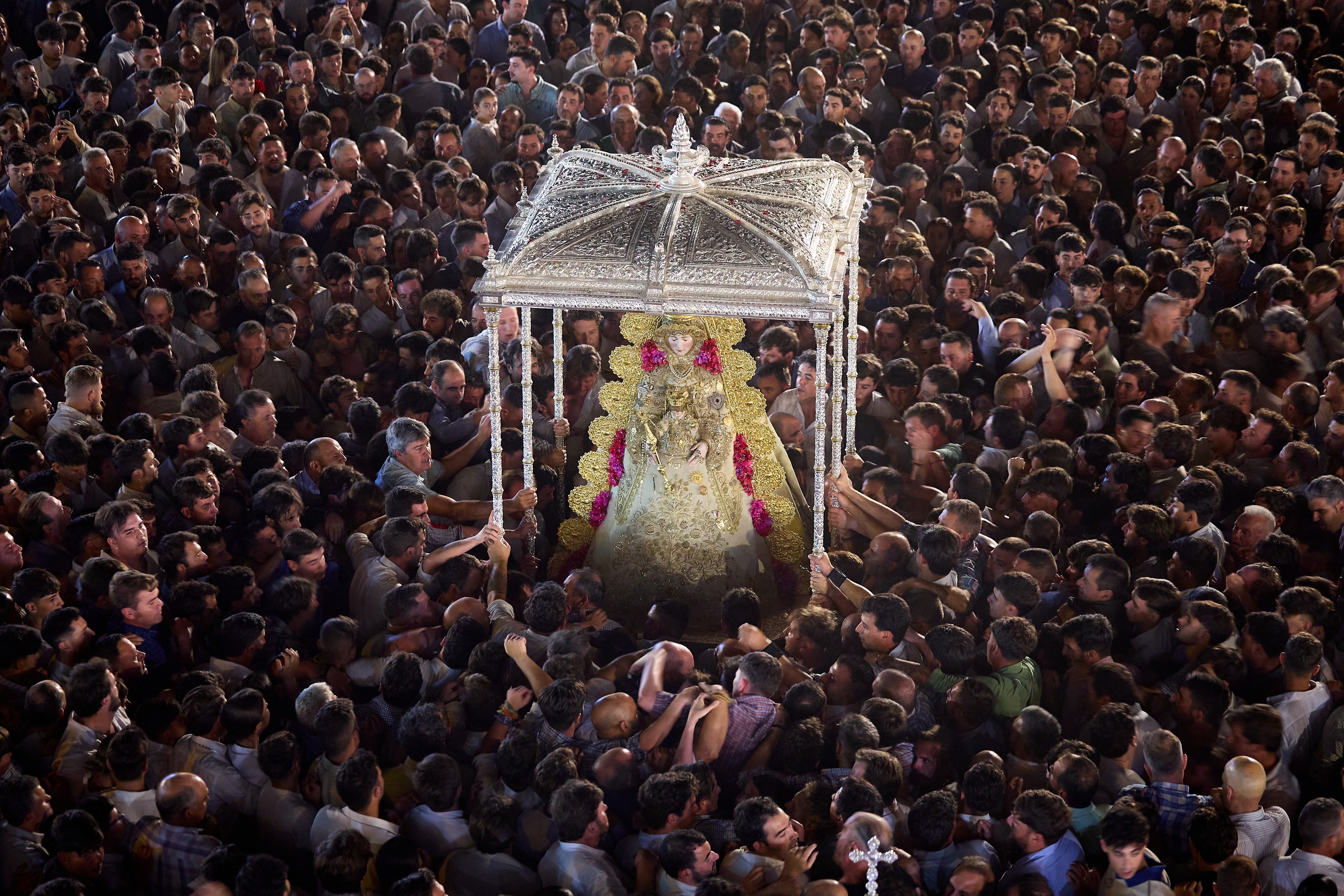 A large crowd of people surround and carry an ornate statue of the Virgin Mary.