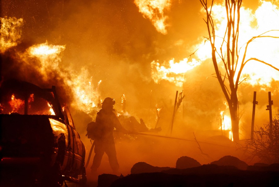 A firefighter sprays water toward a wildfire, with flames all around .