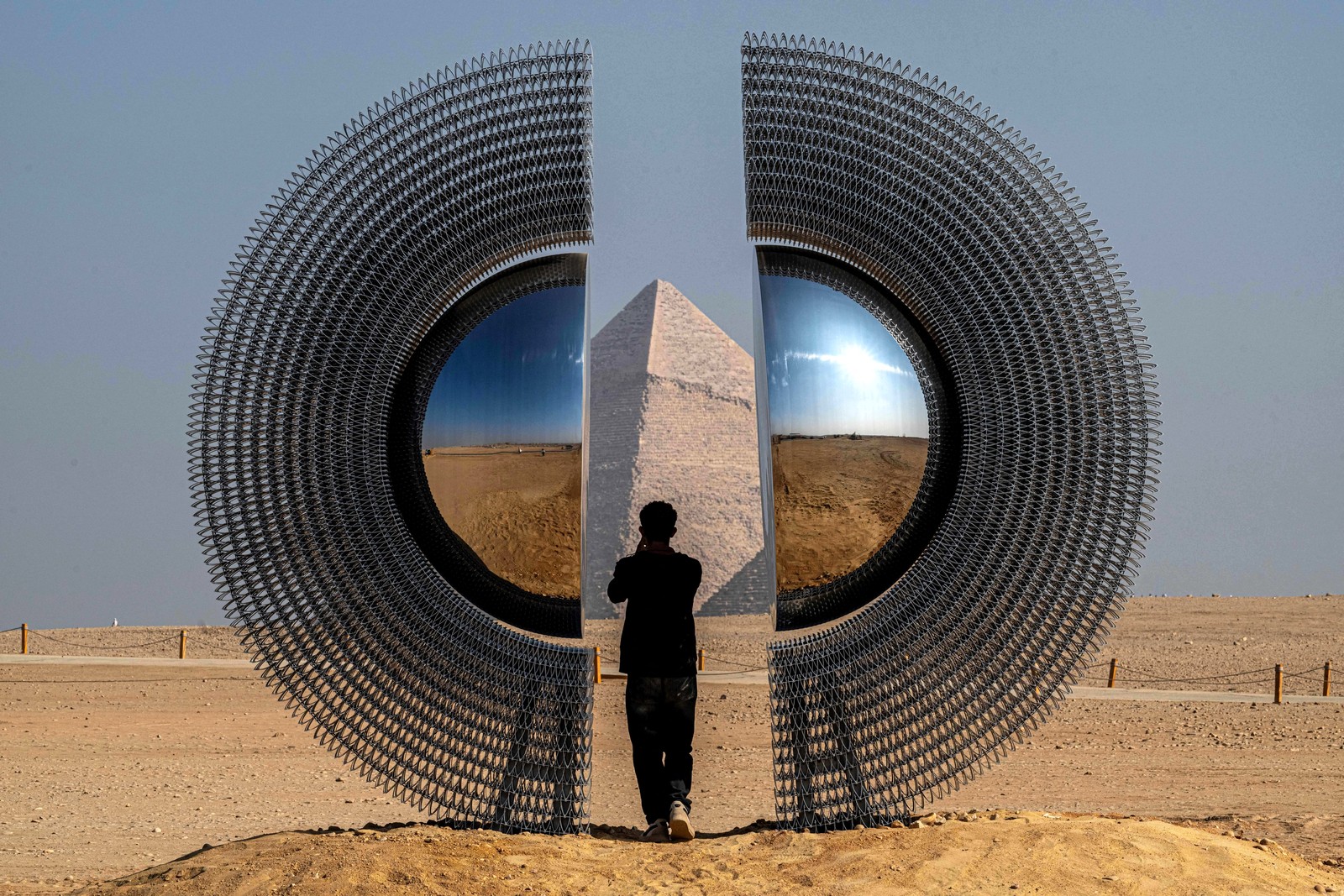 A person stands inside a large circular art installation that has been set up beside the Giza pyramids in Egypt.