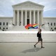 A person flies a pride rainbow flag outside the Supreme Court.