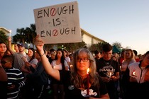 People hold candles at a rally and a woman holds a sign that reads "Enough is enough."