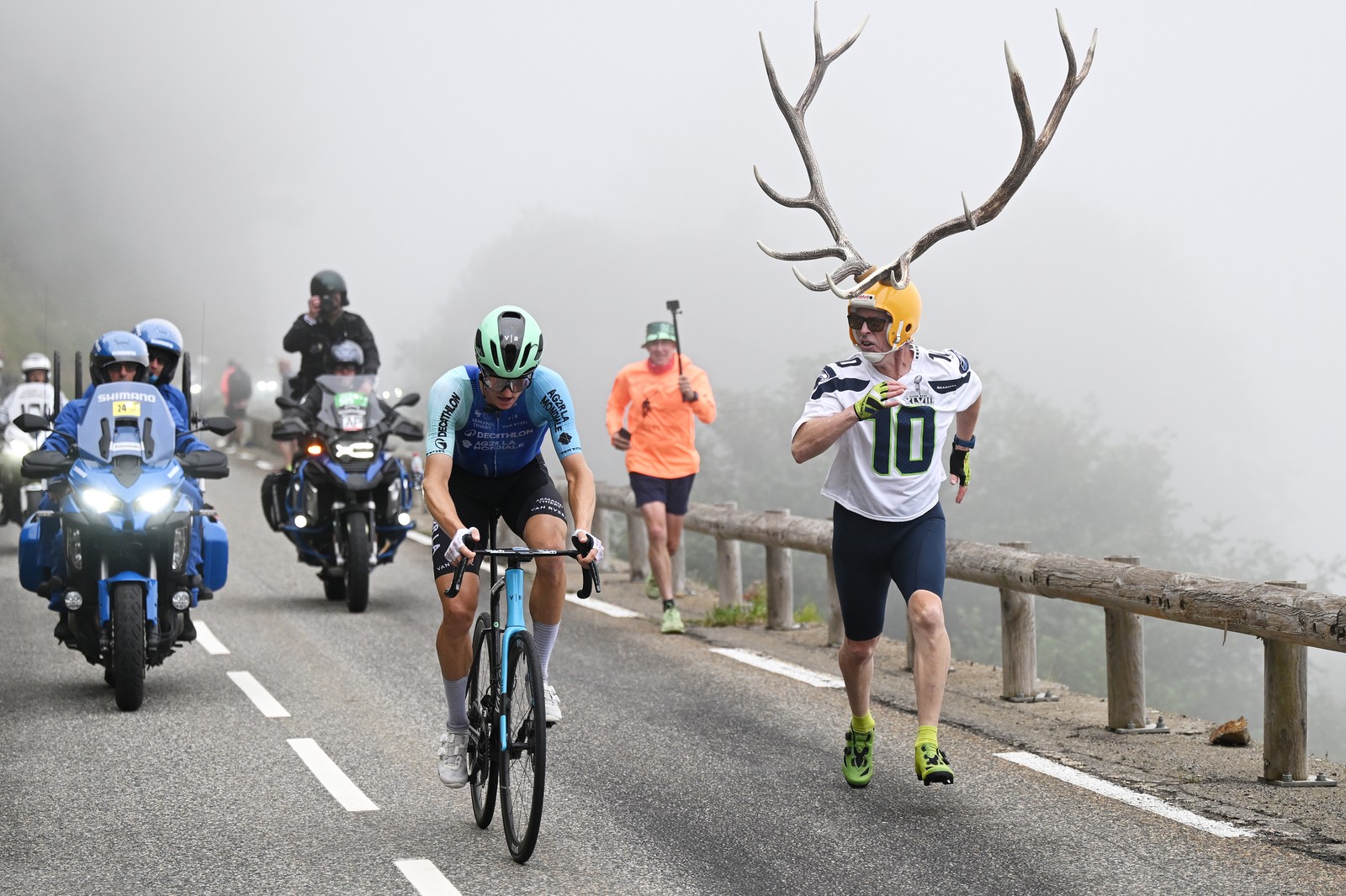 A fan wearing a helmet adorned with gigantic antlers runs beside a cyclist during the Tour de France.