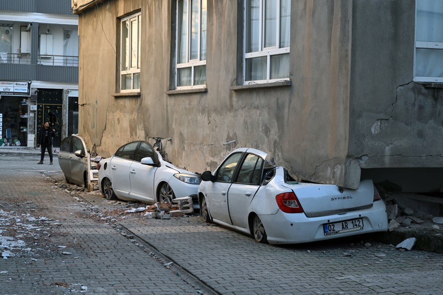 An upper story of a partially collapsed building rests atop three crushed cars.