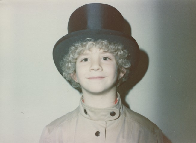 candid photo of smiling young curly-haired kid wearing black top hat