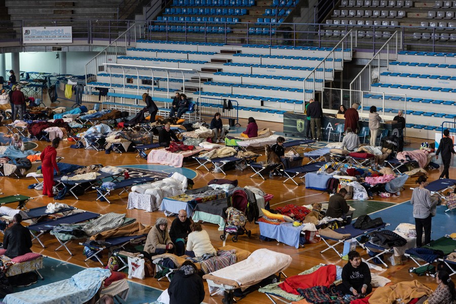 The floor of a sports arena is filled with people and cots.