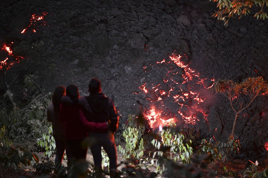People stand near a slow-moving lava flow at night.