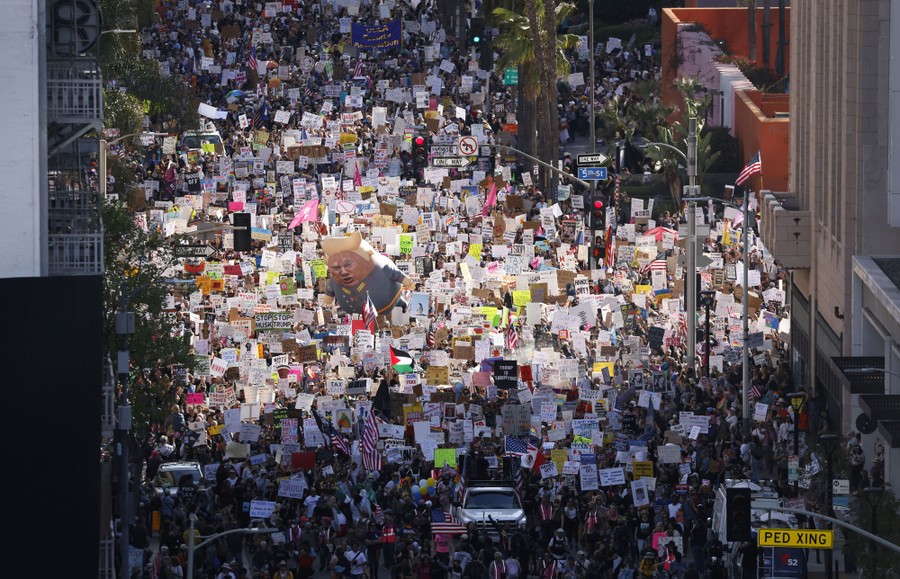 A large crowd of protesters marches down a Los Angeles street carrying many signs.