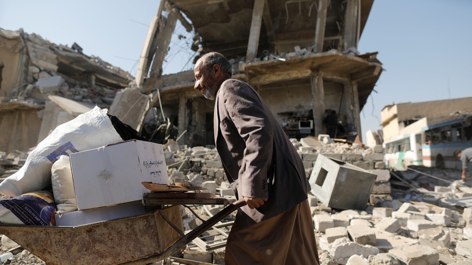 A man walks past a house destroyed during fighting between Iraqi security forces and Islamic State's fighters in Mosul, Iraq, carrying a wheelbarrow loaded with possessions. 