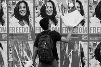 A black-and-white photo of a man tearing down a poster among a spread of identical posters depicting Kamala Harris and the word 'freedom.'
