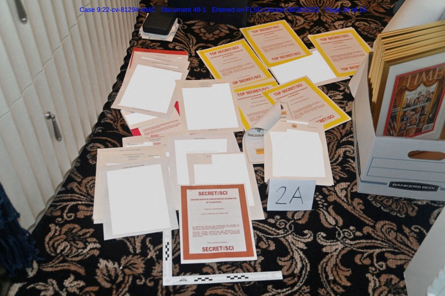 A photograph of a loose pile of documents on a carpeted floor, many covered with sheets labeled "Top Secret"