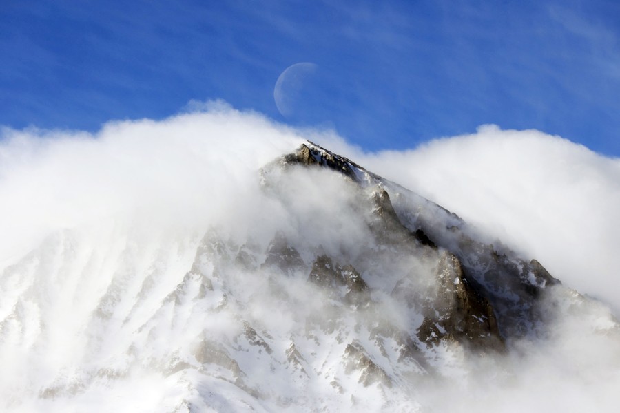 The moon sets over a mountain shrouded in clouds.