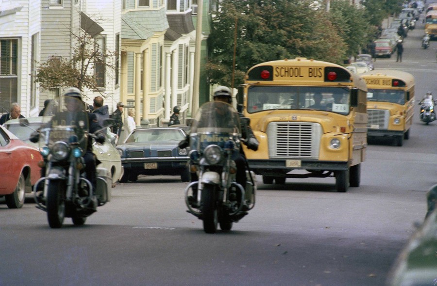 Motorcycle police escort school buses down a street.