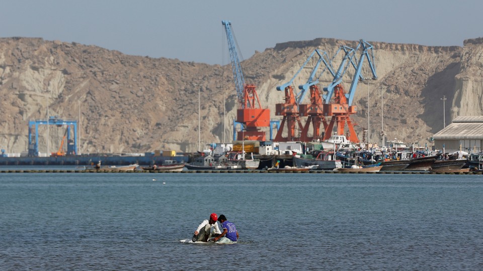 Boys sit on a piece of styrofoam sheet as they search for crabs in front of the Gwadar port in Pakistan.