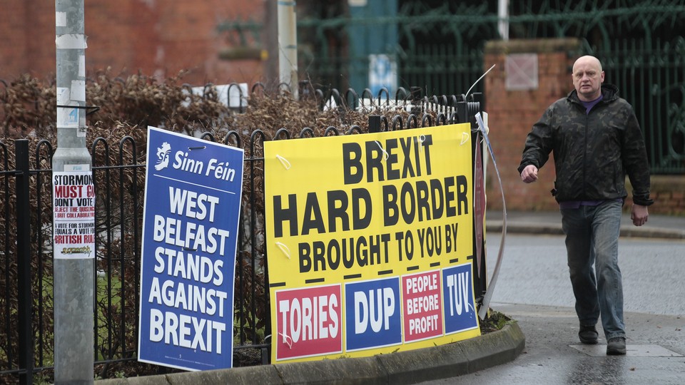 A man walks past posters reading "Brexit Hard Border Brought to You By Tories, DUP" and "West Belfast Stands Against Brexit."