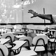 A hand wearing a cleaning glove gestures in a classroom filled with empty tablet-arm chairs.