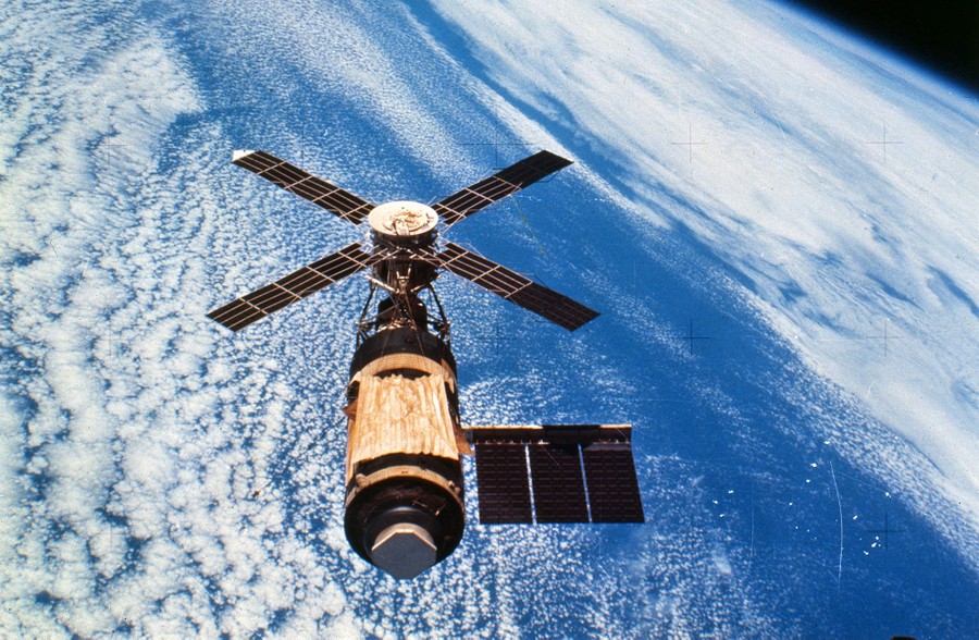 A small space station is seen in Earth orbit above a cloud-covered ocean.