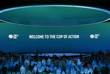 In a blue-lit room a blue and green ombre screen reads "welcome to the COP of action." A large circular blue light defines the ceiling.