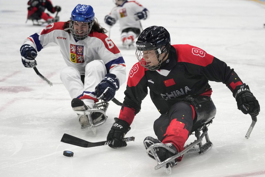 Two hockey players compete for the puck; the player for Team China is in front, with the puck, while the Czech Republic player is close behind, on the left.