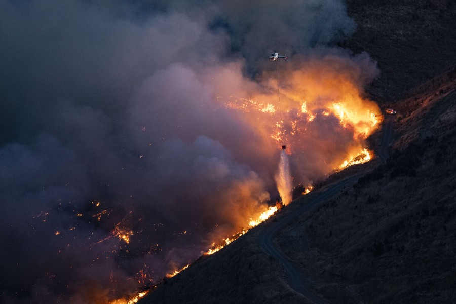 A helicopter drops a bucket of water onto a forest fire.