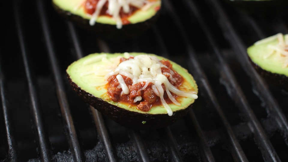 Avocados stuffed with chili sit on a grill.