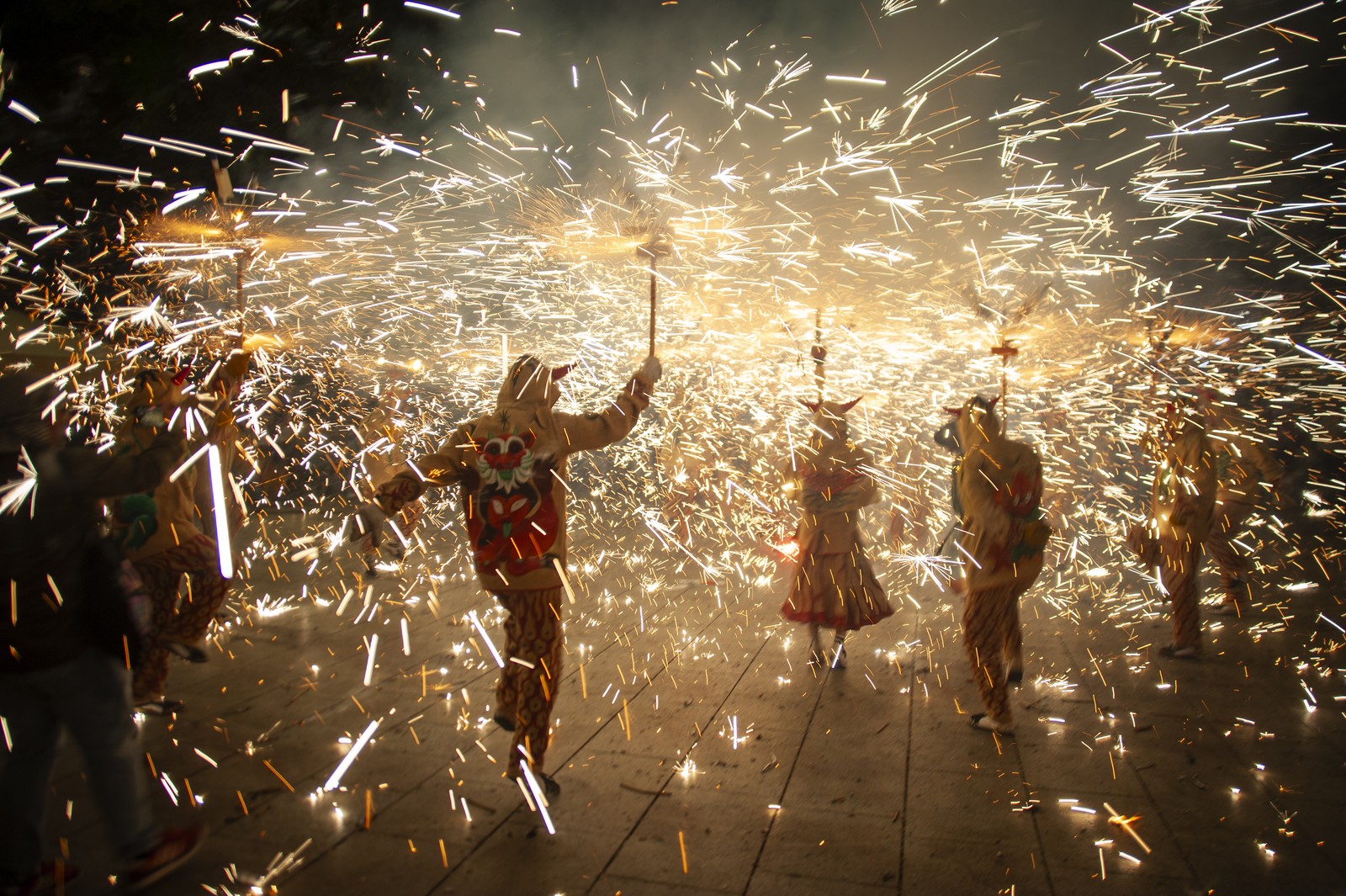 Celebrants carry erupting fireworks on sticks in a plaza.