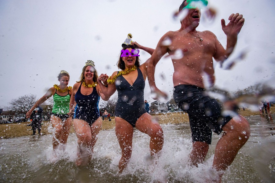 Several revelers wearing New Year's hats and glasses run into the water.