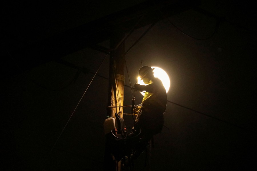 A utility worker is high on a pole, silhouetted by a full moon.