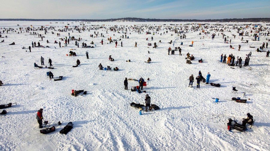 Thousands of people are seen scattered about on a frozen, snow-covered lake, ice fishing.