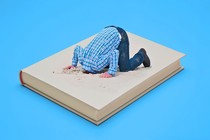 A man sticking his head in a hole in the sand, but the sand is a book