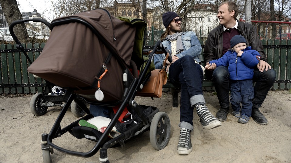 Anders Veide looks on as his friend Set Moklint plays with his child during paternity leave in Stockholm, Sweden.