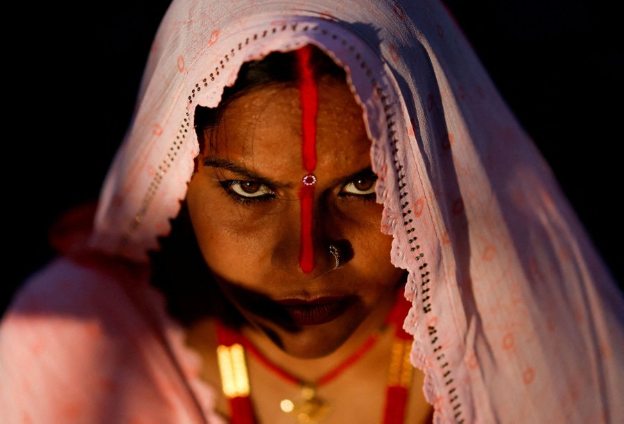 A person looks toward the camera, with red makeup across their forehead and the bridge of their nose.