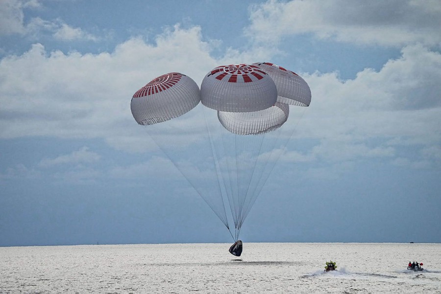 A space capsule held aloft by four parachutes drops into the ocean.