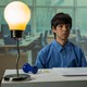Julio Torres sits at a desk with a comically large lightbulb and pushpin