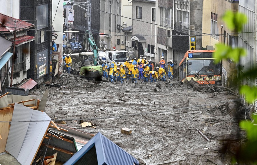 Mud fills a city street, as rescue workers move through the lower end of it.